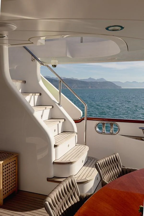 The aft deck features a stylish staircase leading to the upper deck, with a view of the ocean and distant mountains. aboard HOSHI Yacht for Sale
