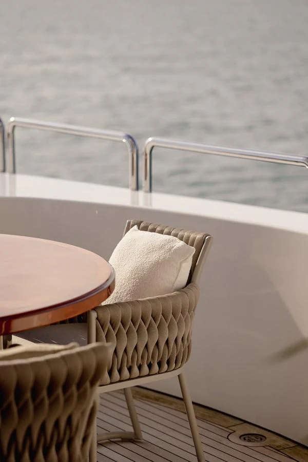 A serene view of a yacht's outdoor seating area with plush chairs and a wooden table, overlooking the calm sea. aboard HOSHI Yacht for Sale