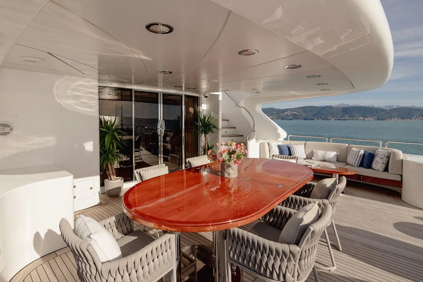 The aft deck features a stylish dining area with a polished wooden table and comfortable seating, offering stunning views of the sea. aboard HOSHI Yacht for Sale