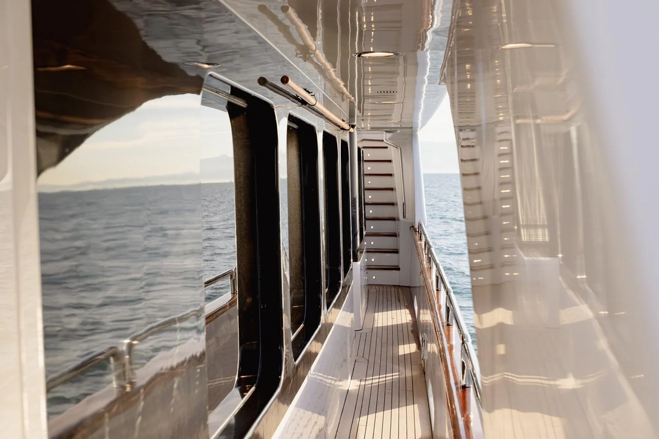 The side deck of the yacht offers a sleek and reflective passageway with a view of the sea. aboard HOSHI Yacht for Sale