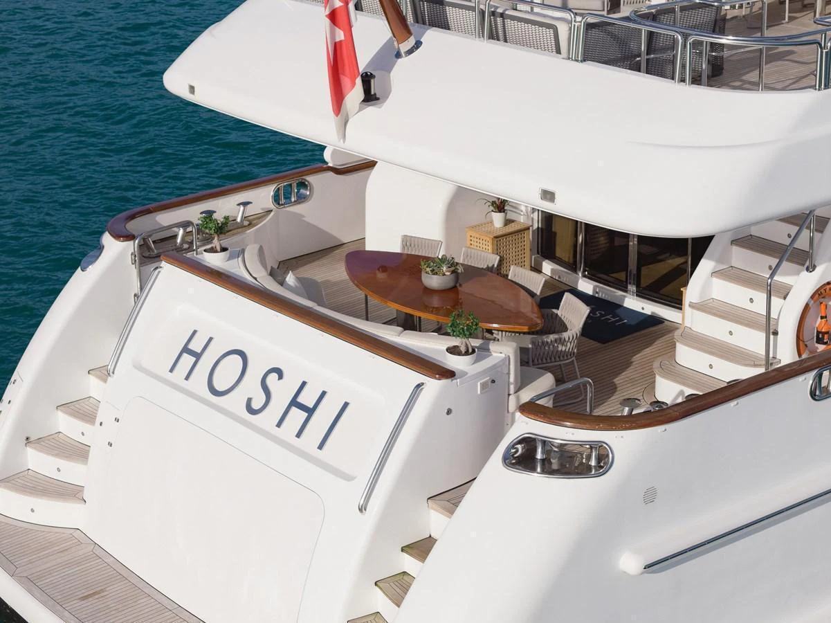The aft deck of the yacht features a stylish seating area with a wooden table, perfect for alfresco dining. aboard HOSHI Yacht for Sale