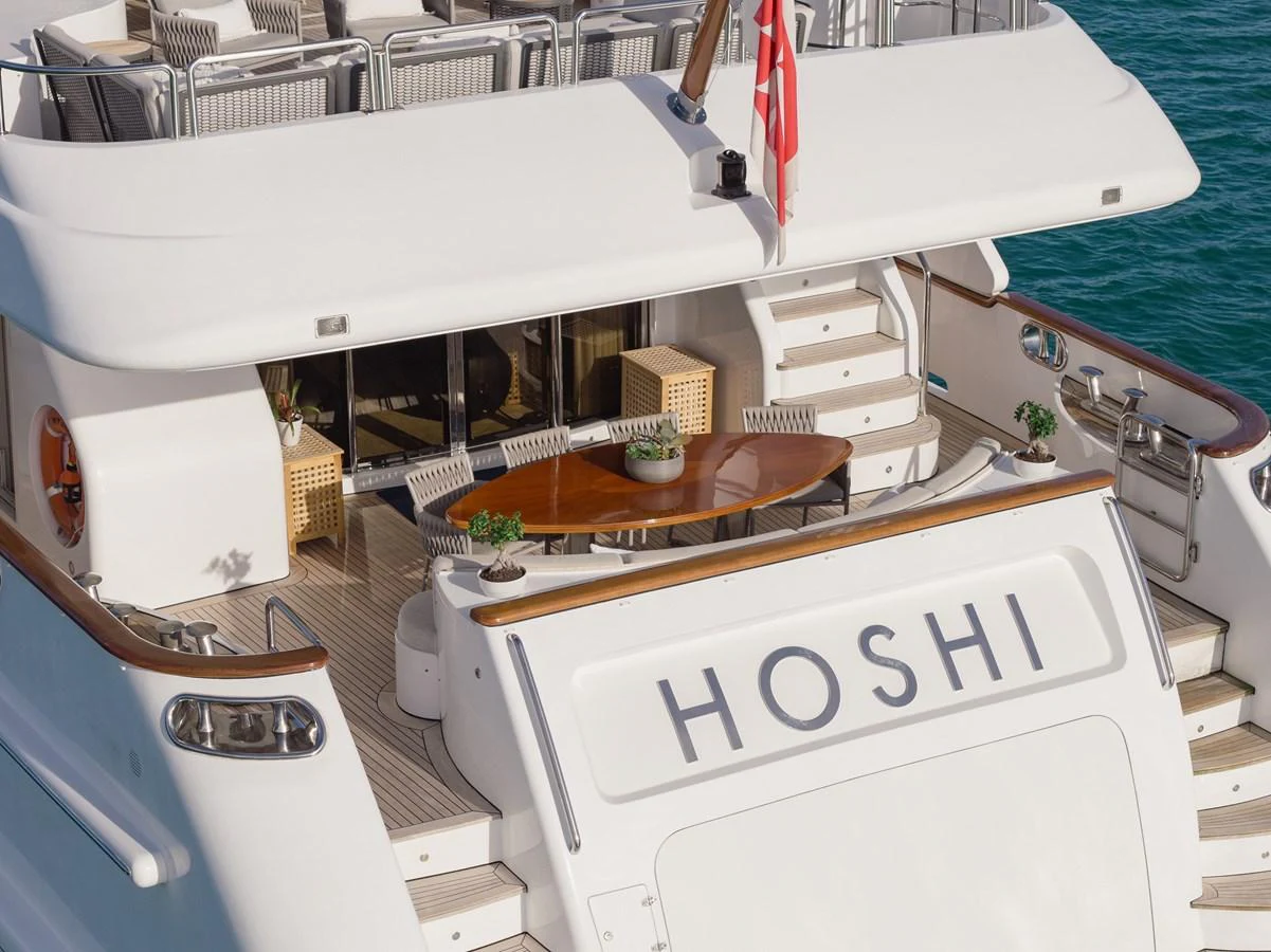 The aft deck features a stylish dining area with a polished wooden table and comfortable seating, perfect for alfresco dining. aboard HOSHI Yacht for Sale