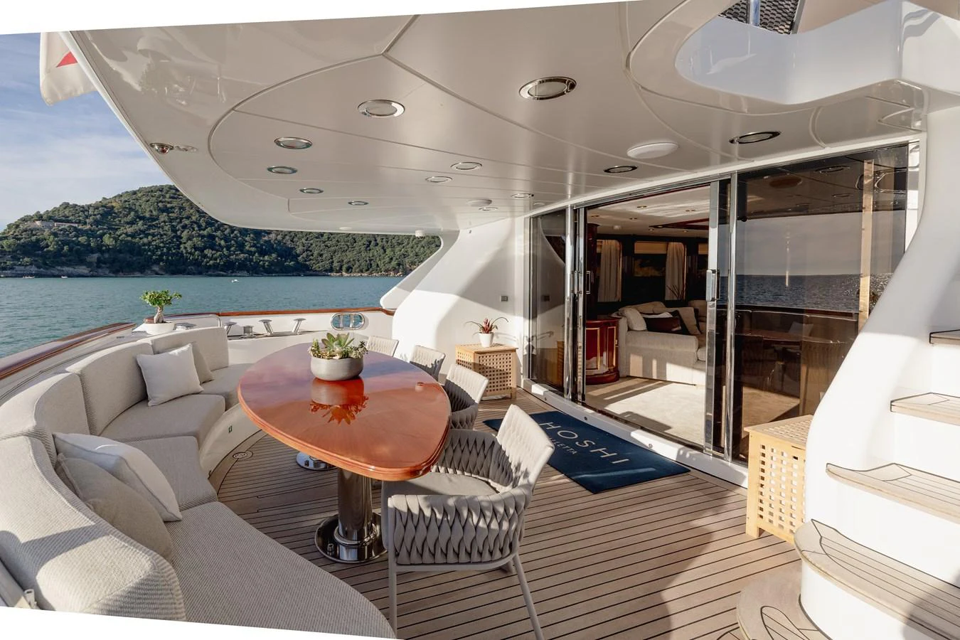 The aft deck features a spacious seating area with a polished wooden table and comfortable chairs, perfect for outdoor dining and relaxation. aboard HOSHI Yacht for Sale