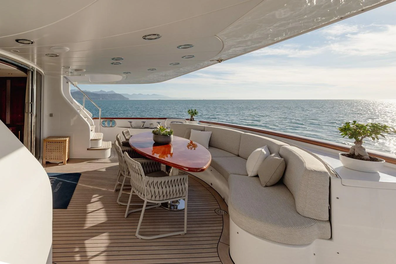 The aft deck features a stylish seating area with a curved sofa and a polished wooden table, perfect for enjoying ocean views. aboard HOSHI Yacht for Sale
