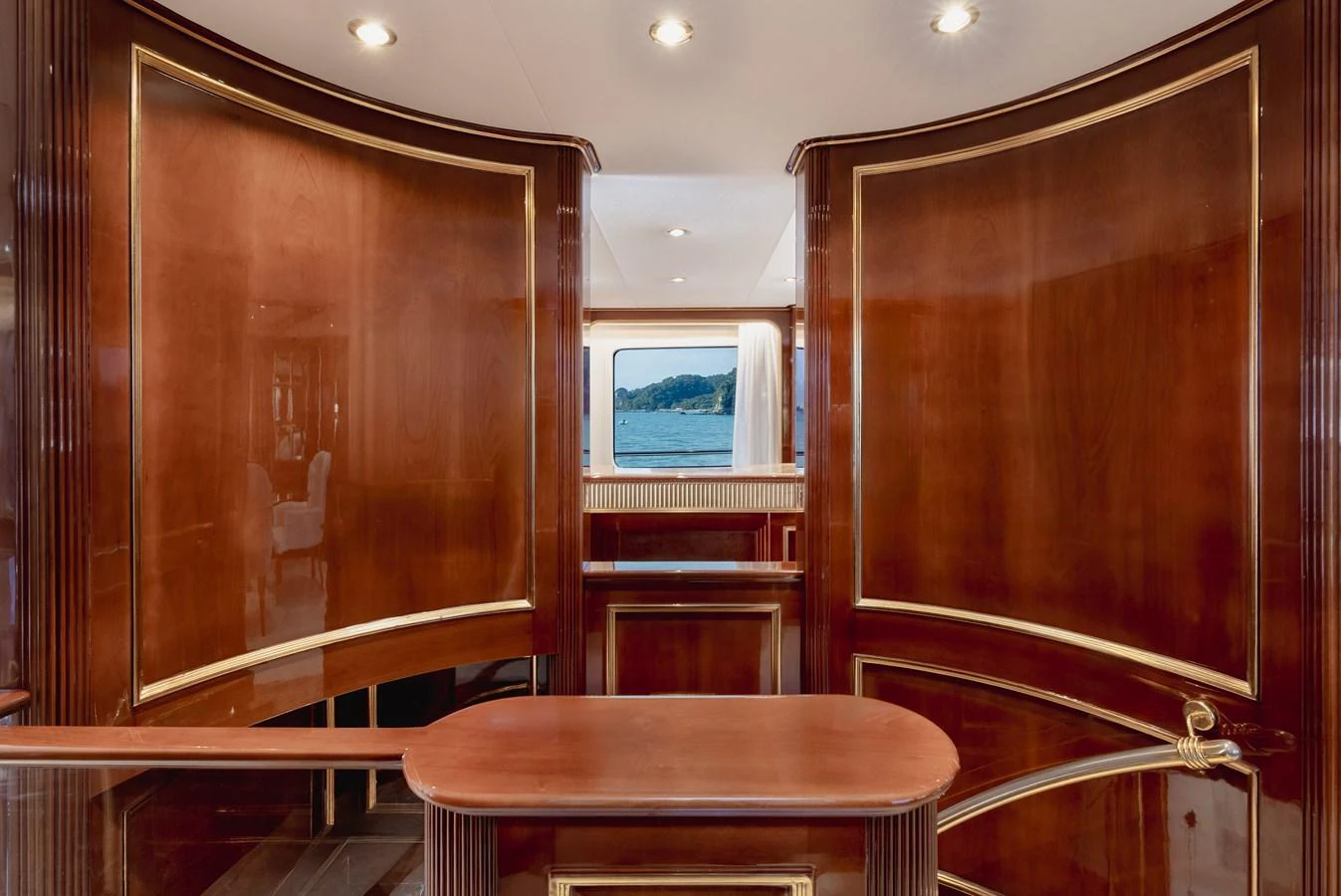 The yacht's interior features elegant wood paneling with gold accents and a view of the sea through a window. aboard HOSHI Yacht for Sale