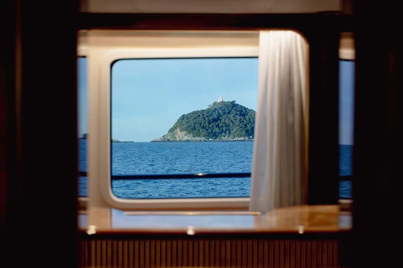 A serene view of the sea and a distant island through a yacht's window. aboard HOSHI Yacht for Sale