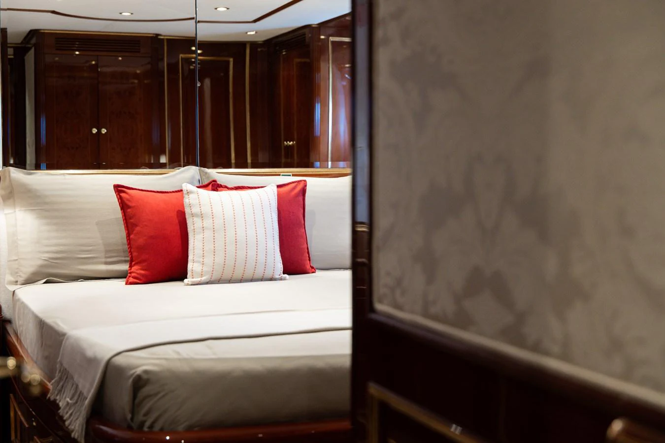A luxurious stateroom featuring a plush bed with red accent pillows and elegant wood paneling. aboard HOSHI Yacht for Sale