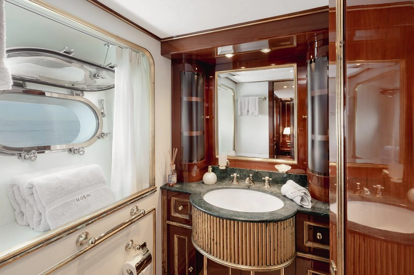The yacht's bathroom features elegant wood finishes and a porthole window with a view of the sea. aboard HOSHI Yacht for Sale