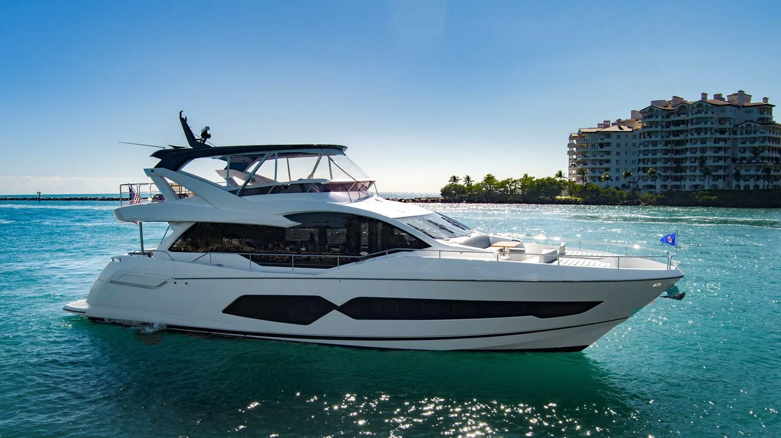 A sleek and modern yacht cruising in clear blue waters near a coastal development. aboard MISTY K Yacht for Sale