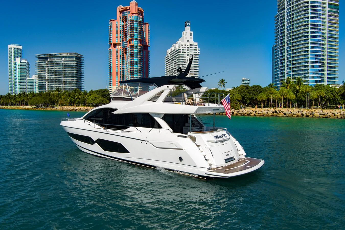 A sleek, modern yacht cruises through a vibrant cityscape with towering buildings in the background. aboard MISTY K Yacht for Sale