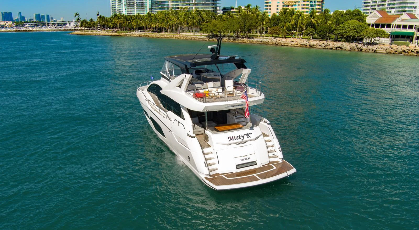 A sleek yacht cruises through calm waters with a scenic city backdrop. aboard MISTY K Yacht for Sale