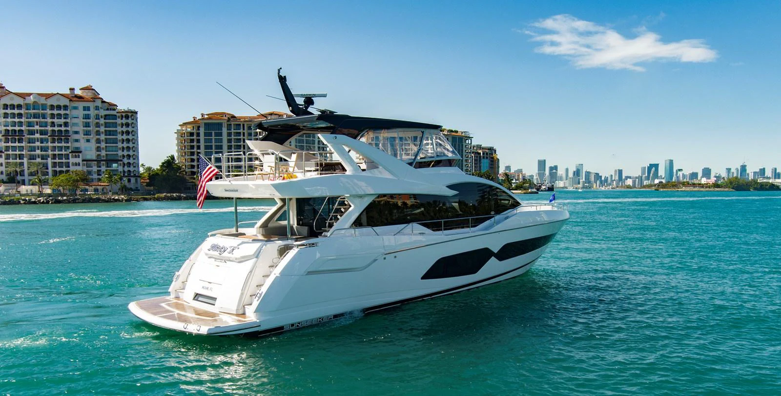 A sleek yacht cruises through vibrant blue waters near a coastal cityscape. aboard MISTY K Yacht for Sale
