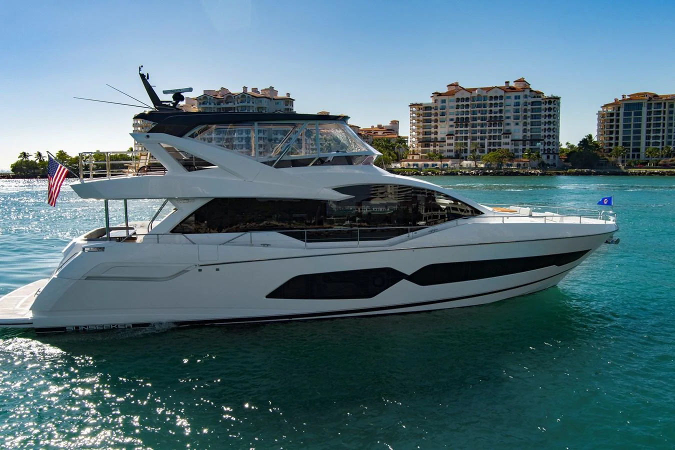 A sleek yacht cruises in a sunny coastal area with modern buildings in the background. aboard MISTY K Yacht for Sale