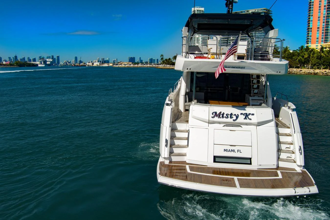 The yacht is cruising away from the shore, showcasing its spacious aft deck and elegant design. aboard MISTY K Yacht for Sale