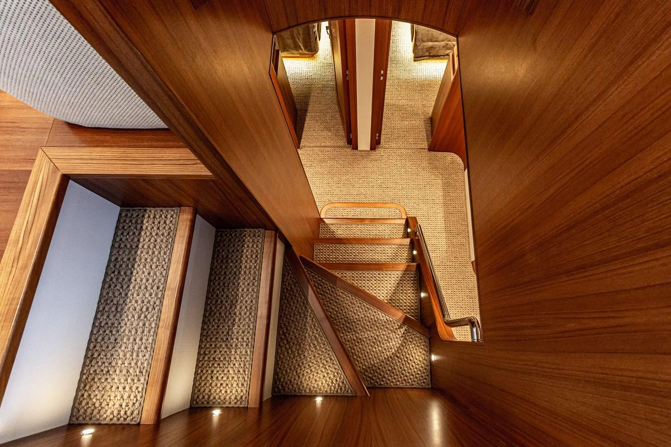 A beautifully crafted wooden staircase leads to the lower deck, showcasing luxurious carpeting and warm lighting. aboard MARIPOSA Yacht for Sale