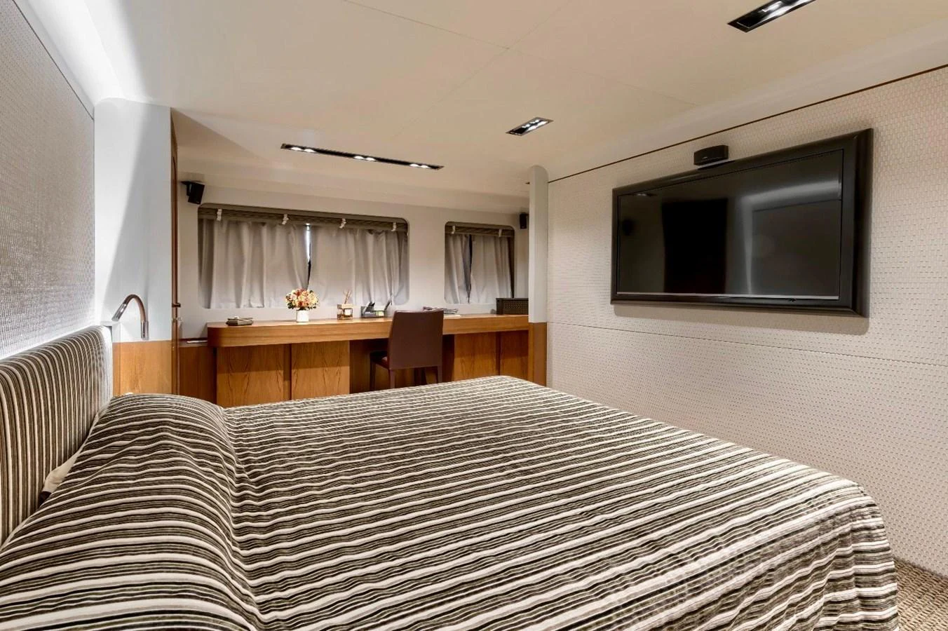 The stateroom features a comfortable bed, a desk area, and a mounted television, creating a cozy and functional space. aboard MARIPOSA Yacht for Sale