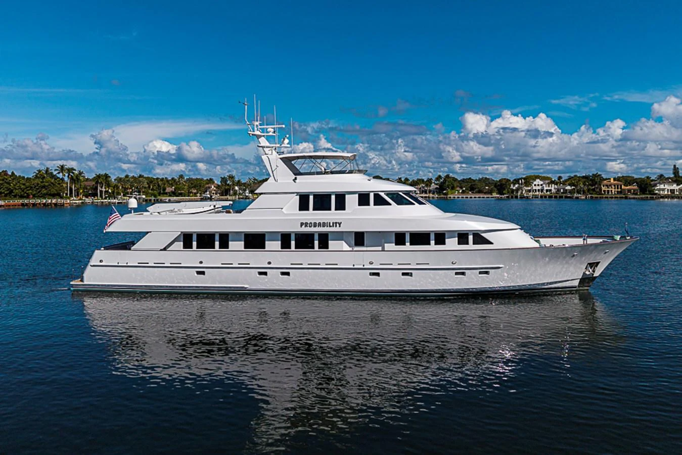 A sleek and elegant yacht is cruising on calm waters under a clear blue sky. aboard PROBABILITY Yacht for Sale