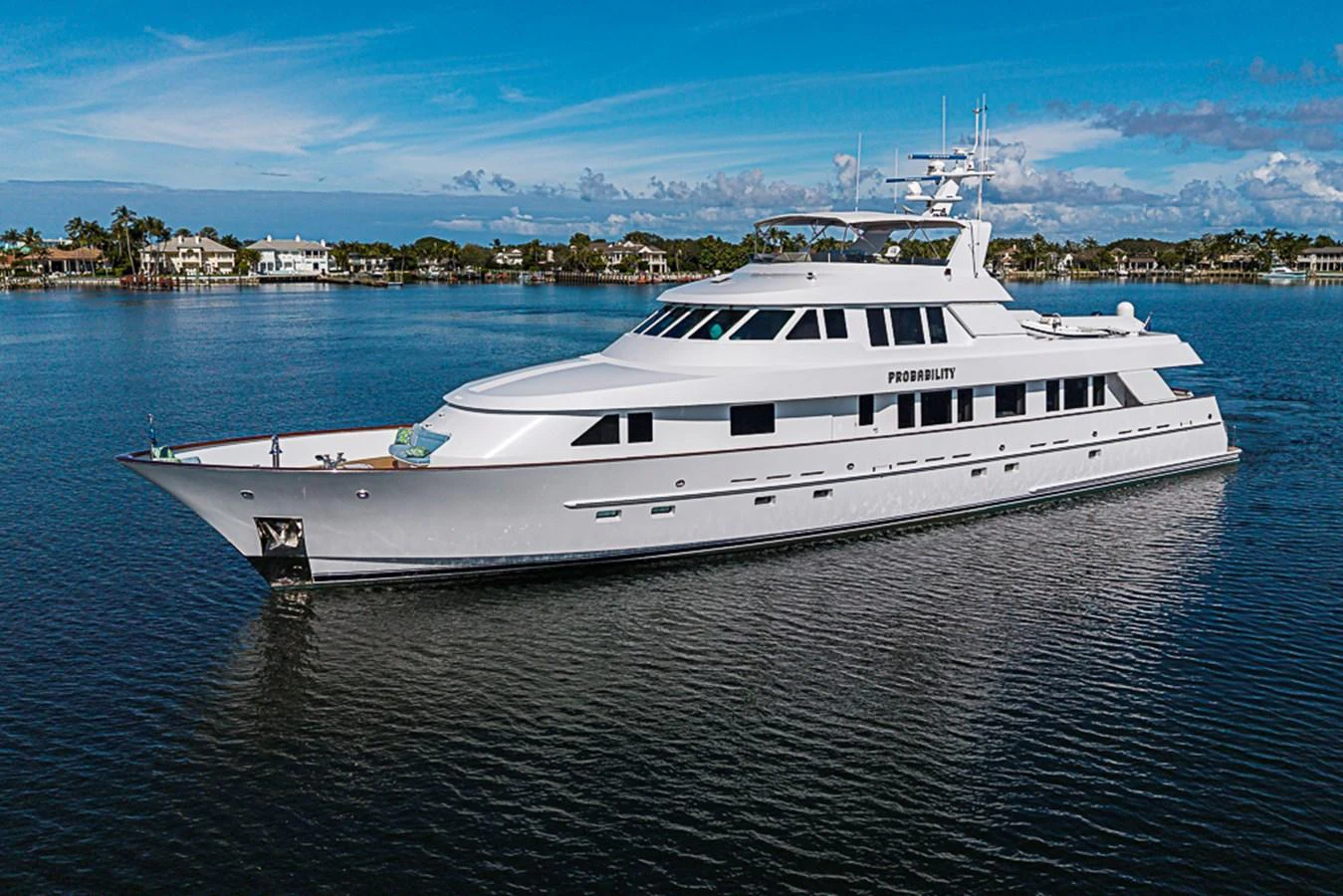 A sleek and elegant yacht glides gracefully on calm waters with a picturesque shoreline in the background. aboard PROBABILITY Yacht for Sale