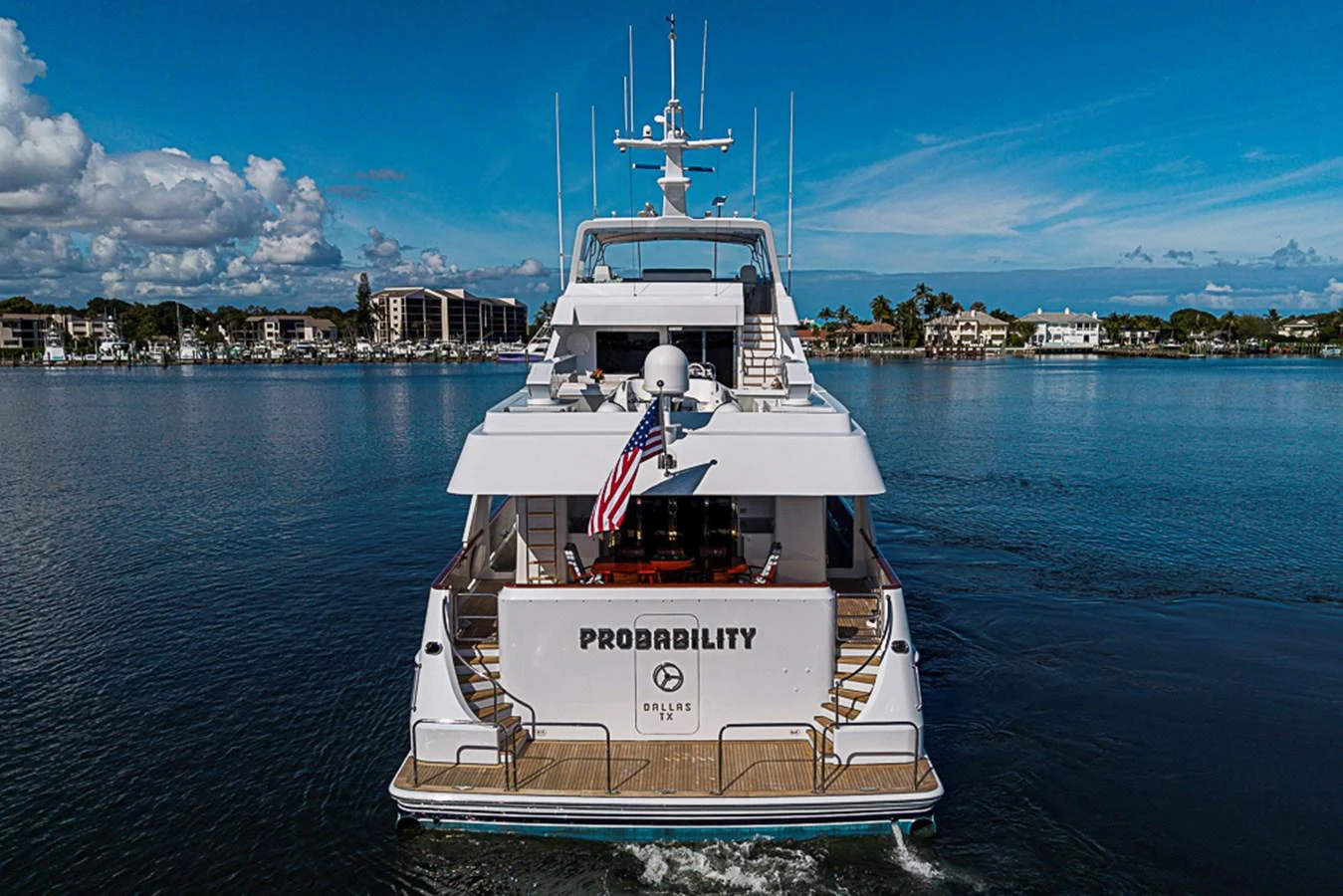 A luxurious yacht is seen from the rear, cruising on calm waters with a clear sky above. aboard PROBABILITY Yacht for Sale