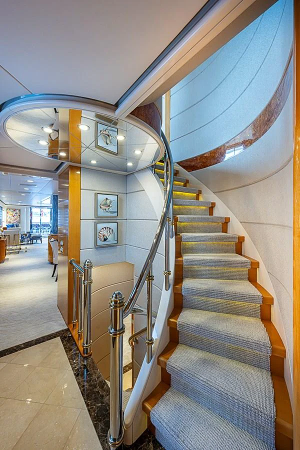 A luxurious staircase with polished railings leads to the upper deck, showcasing elegant decor and artwork. aboard PROBABILITY Yacht for Sale