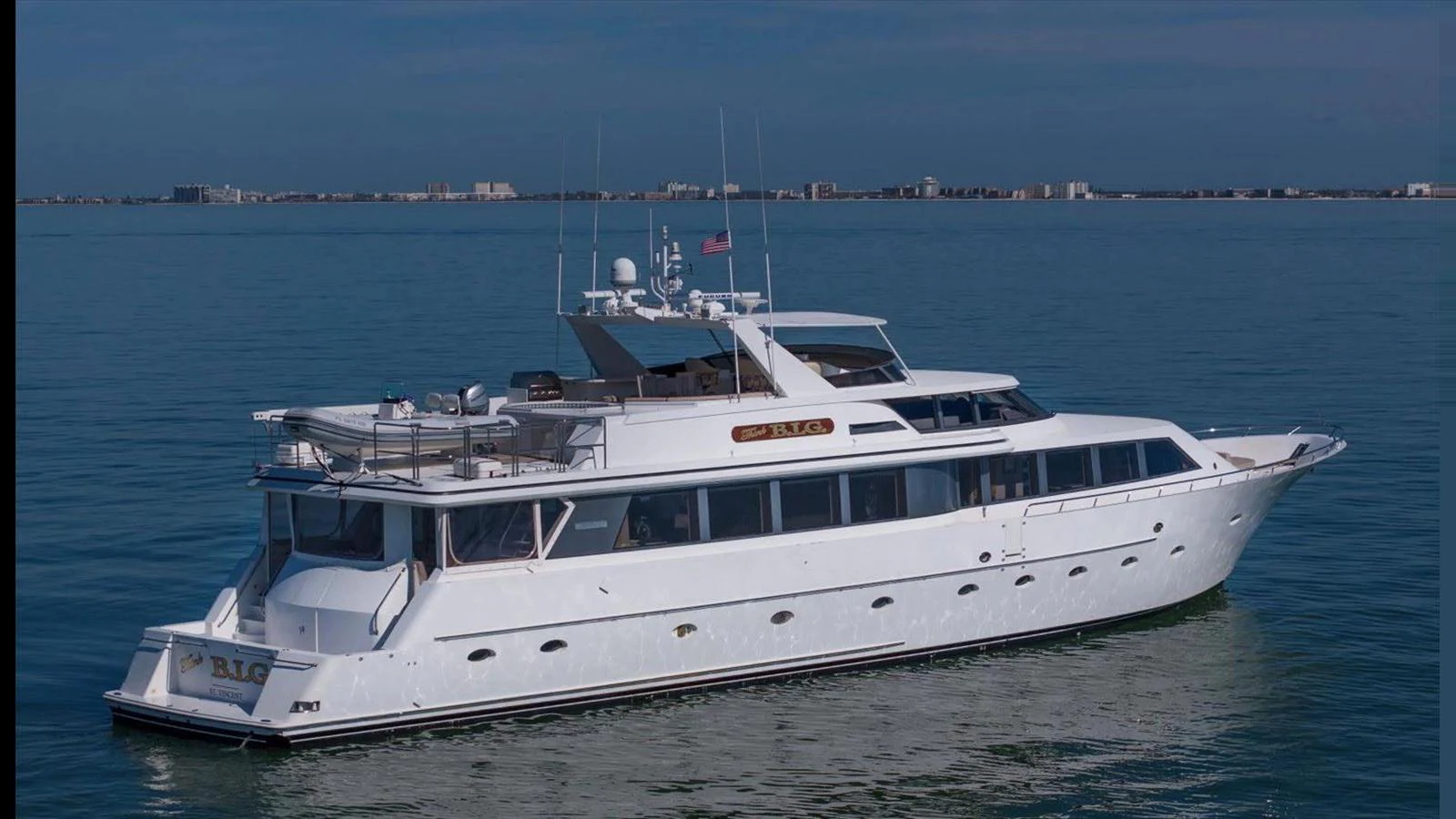 A sleek and elegant yacht cruising on calm waters with a cityscape in the background. aboard THINK B.I.G Yacht for Sale