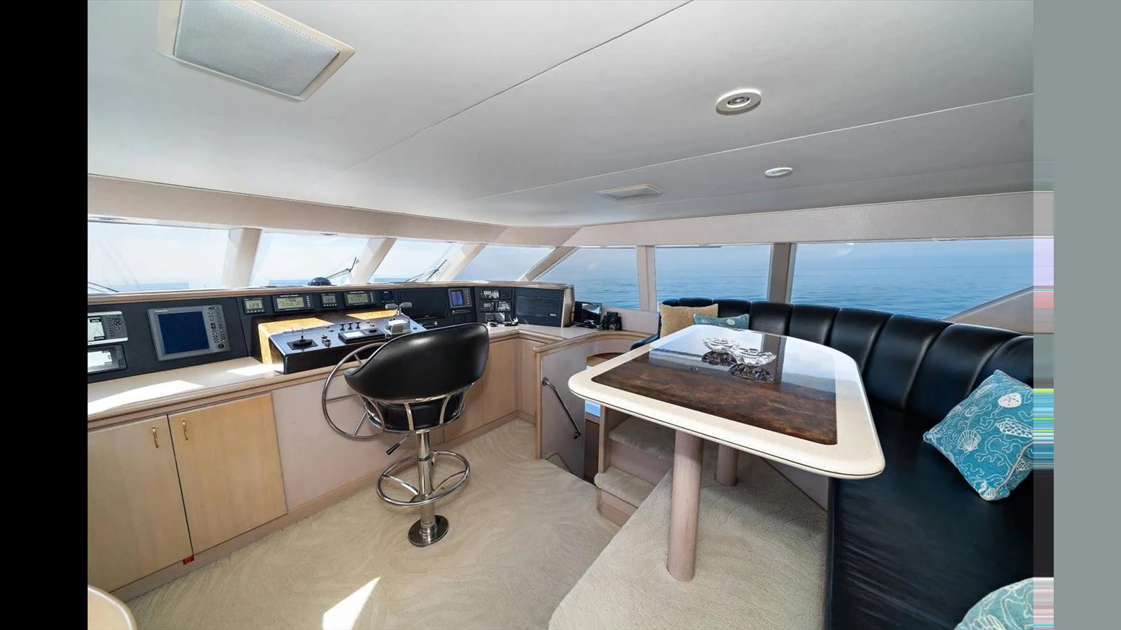 The helm area features a sleek control station and a comfortable seating arrangement with a table. aboard THINK B.I.G Yacht for Sale