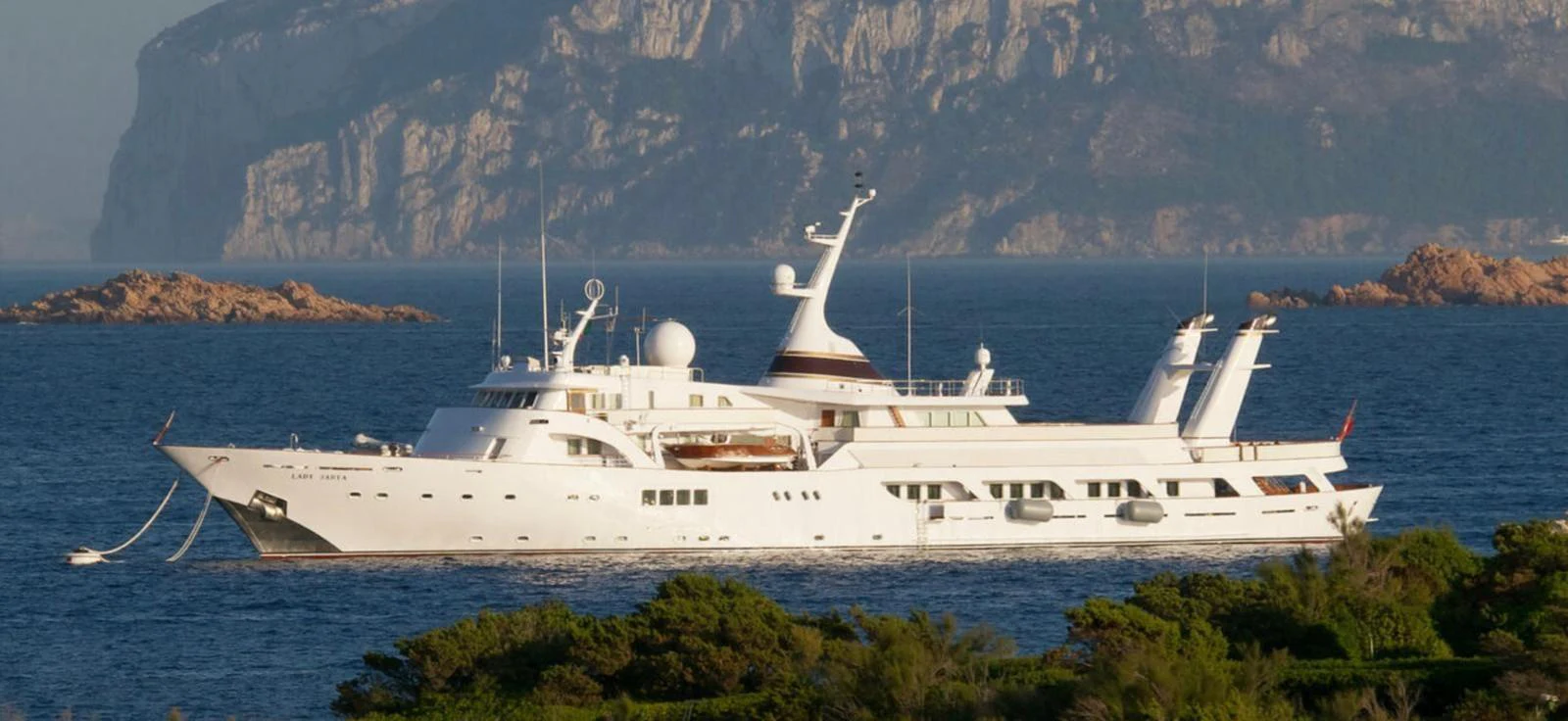 A luxurious yacht glides gracefully on serene waters with a stunning mountainous backdrop. aboard LADY SARYA Yacht for Sale