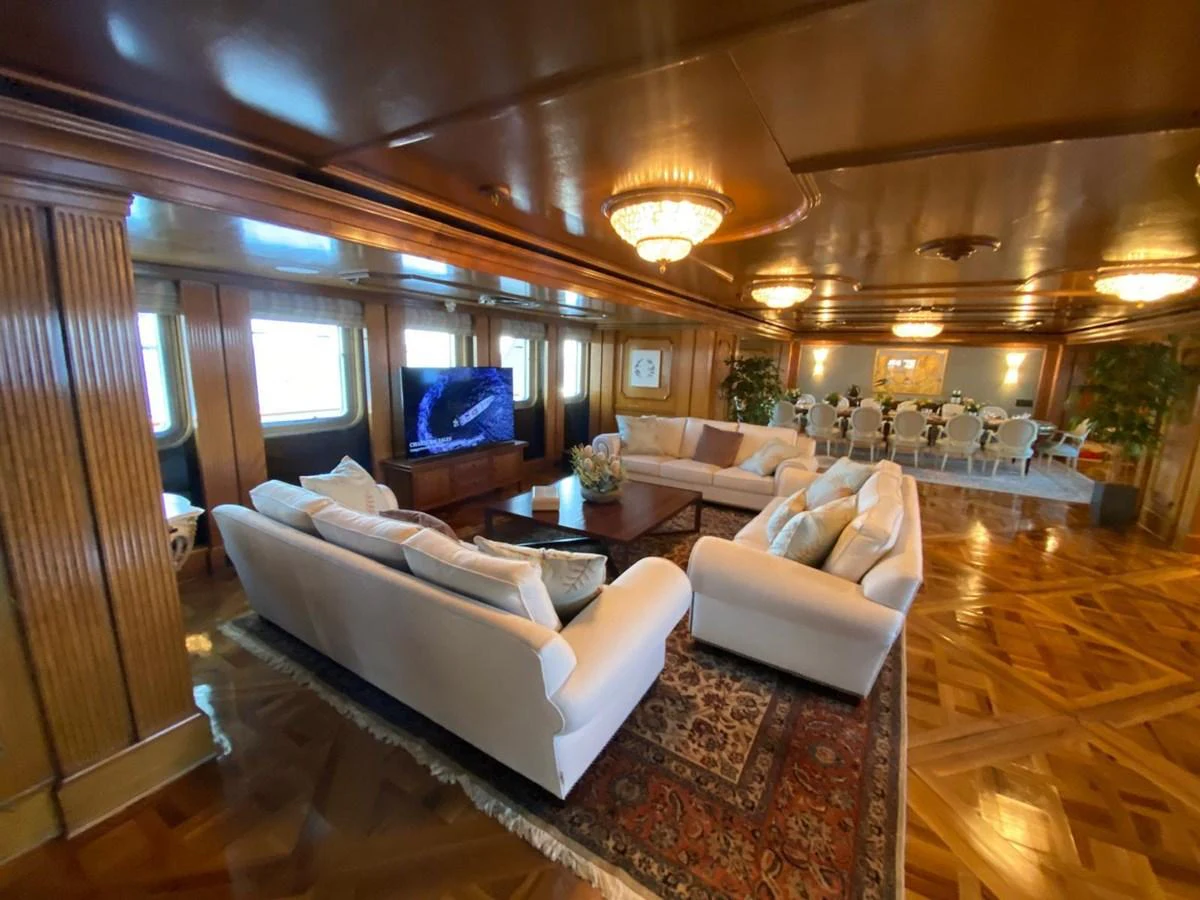 The luxurious salon features elegant seating, a large television, and a formal dining area, all bathed in warm lighting. aboard LADY SARYA Yacht for Sale