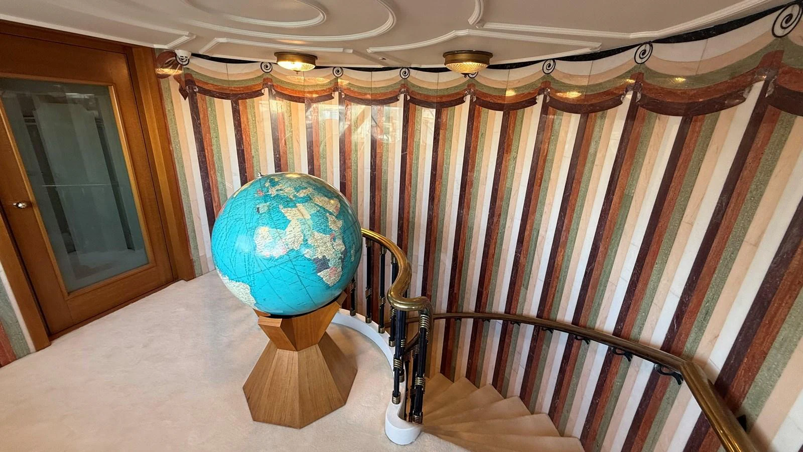 A luxurious interior staircase featuring a large globe and elegant decor. aboard LADY SARYA Yacht for Sale