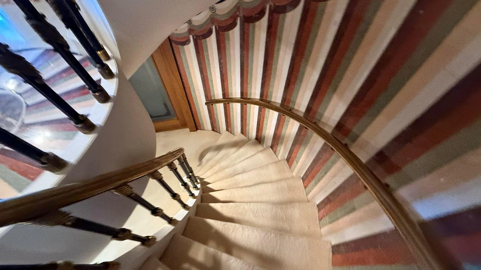 A beautifully designed spiral staircase with a colorful striped carpet and elegant wooden railings. aboard LADY SARYA Yacht for Sale