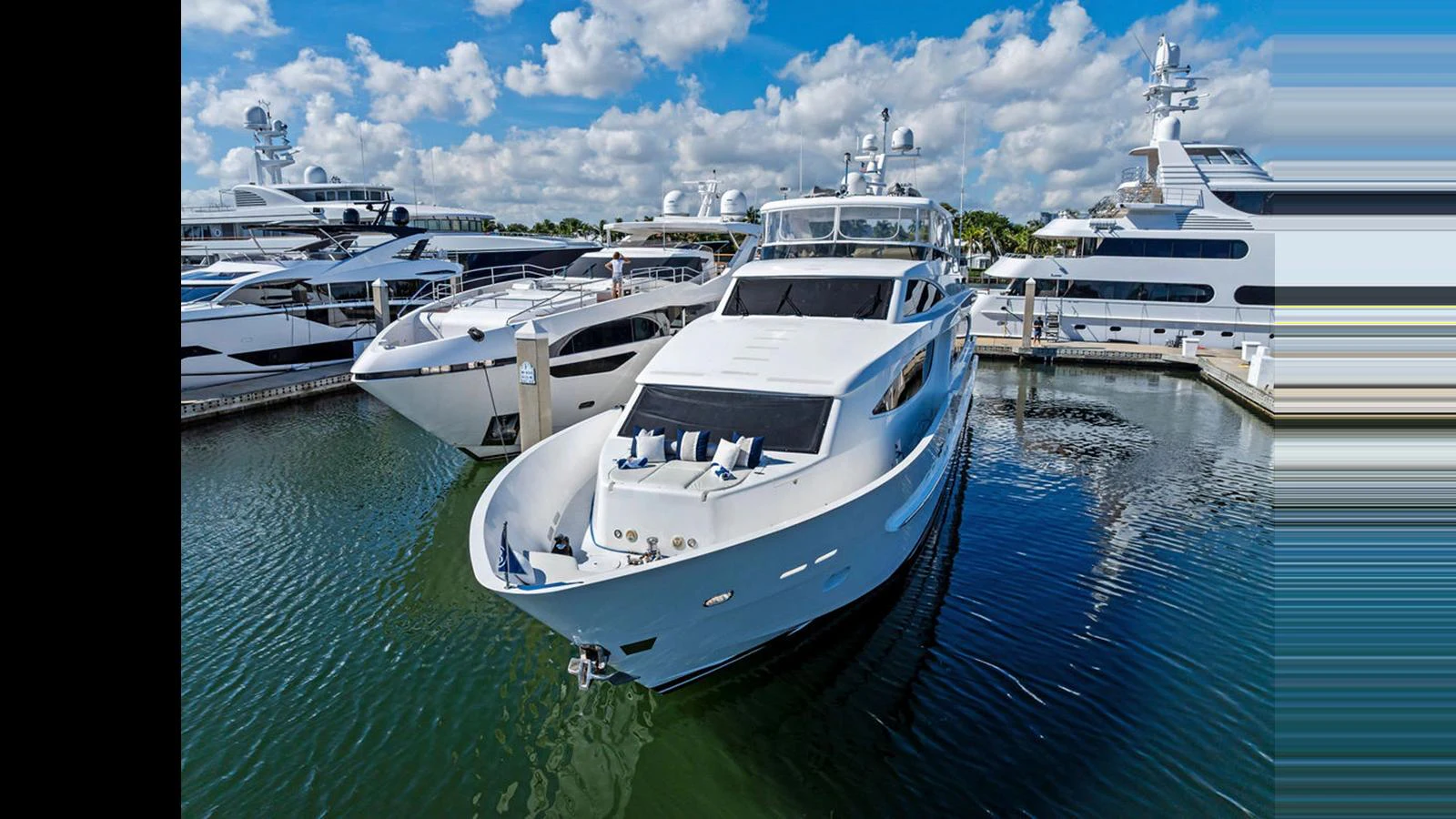 A sleek, modern yacht is docked at a marina, surrounded by other luxury vessels under a bright blue sky with scattered clouds. aboard PERFECT HARMONY Yacht for Sale