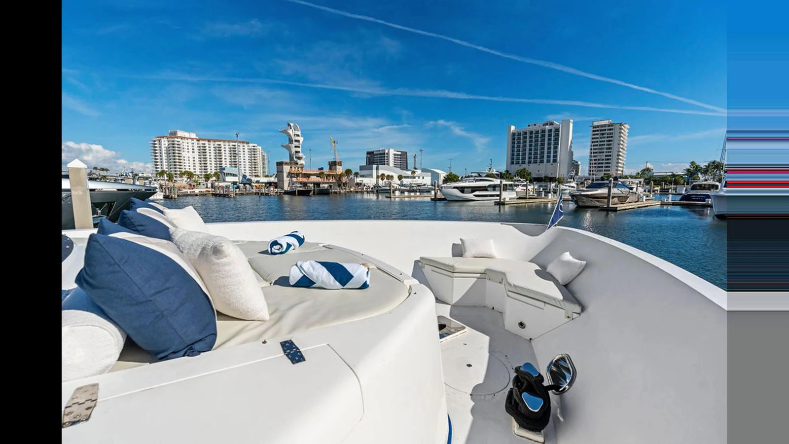 The yacht's bow area offers a comfortable lounging space with plush cushions, set against a backdrop of a vibrant marina. aboard PERFECT HARMONY Yacht for Sale