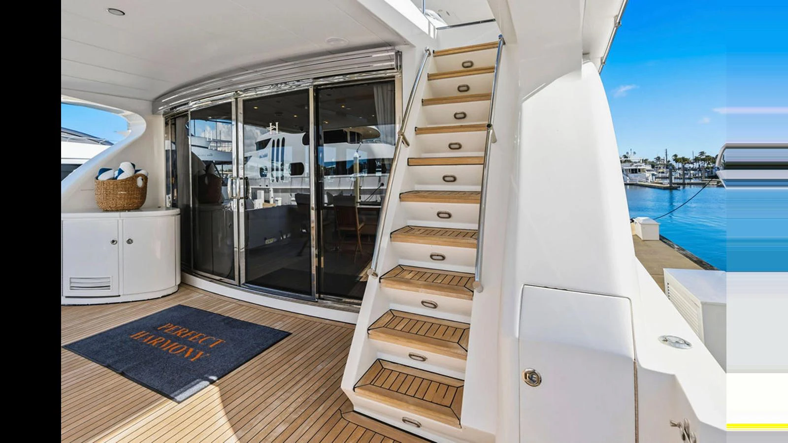 The aft deck features a stylish staircase leading to the upper deck, with a welcoming mat and sleek sliding doors opening to the interior. aboard PERFECT HARMONY Yacht for Sale