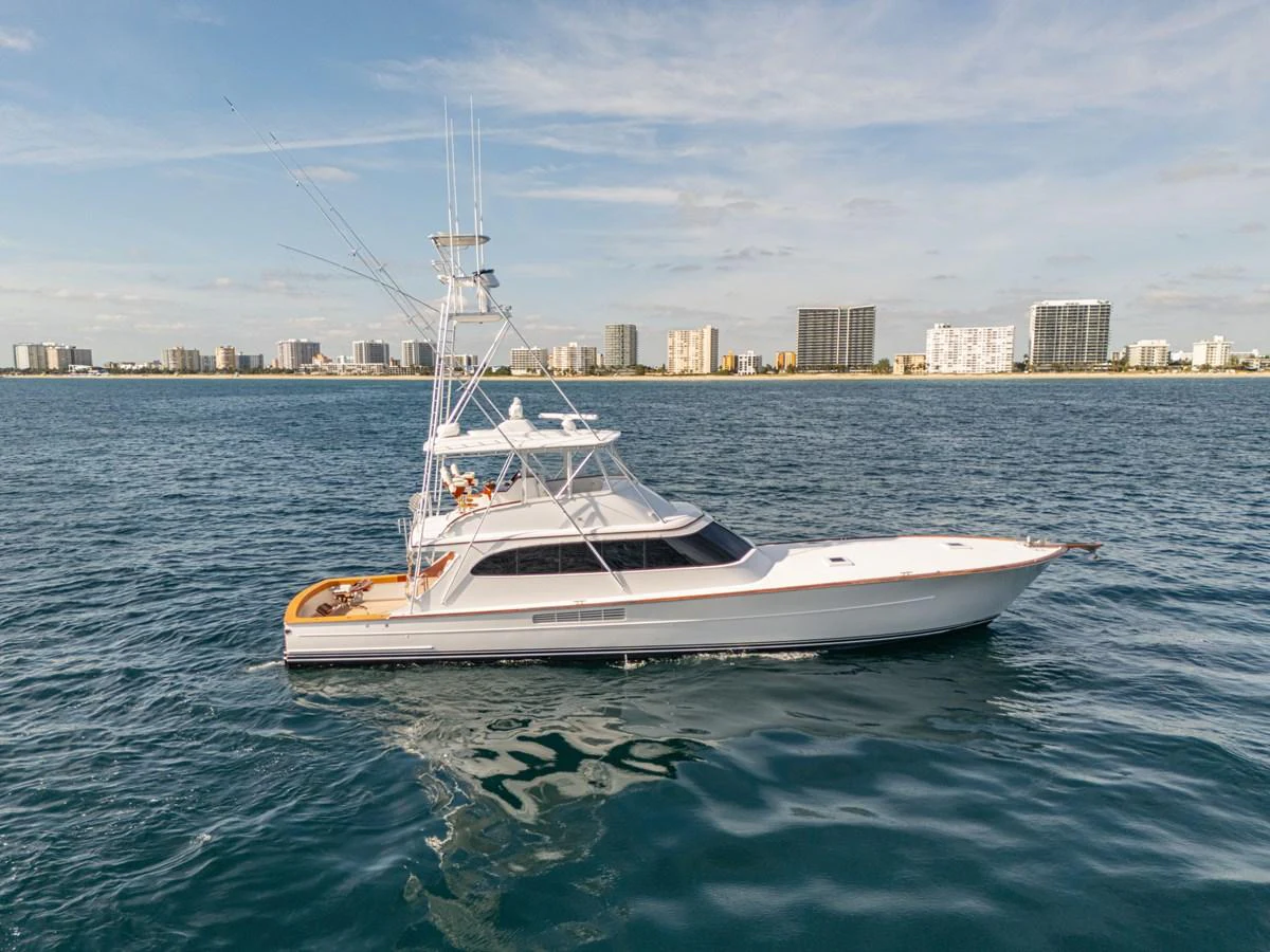 A sleek yacht cruises on calm waters with a cityscape in the background. aboard HT HOOK Yacht for Sale