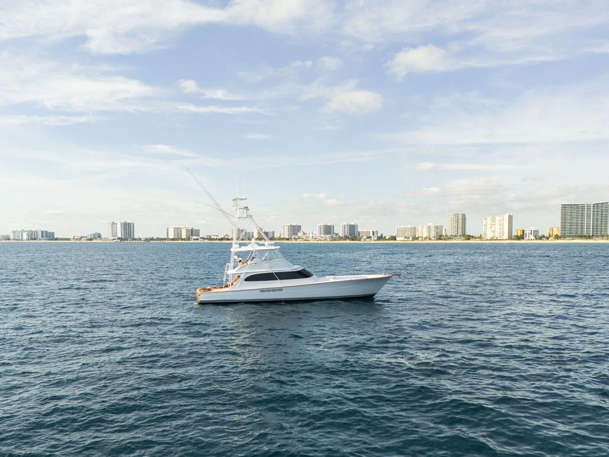 A sleek yacht cruises on calm waters with a cityscape in the background. aboard HT HOOK Yacht for Sale