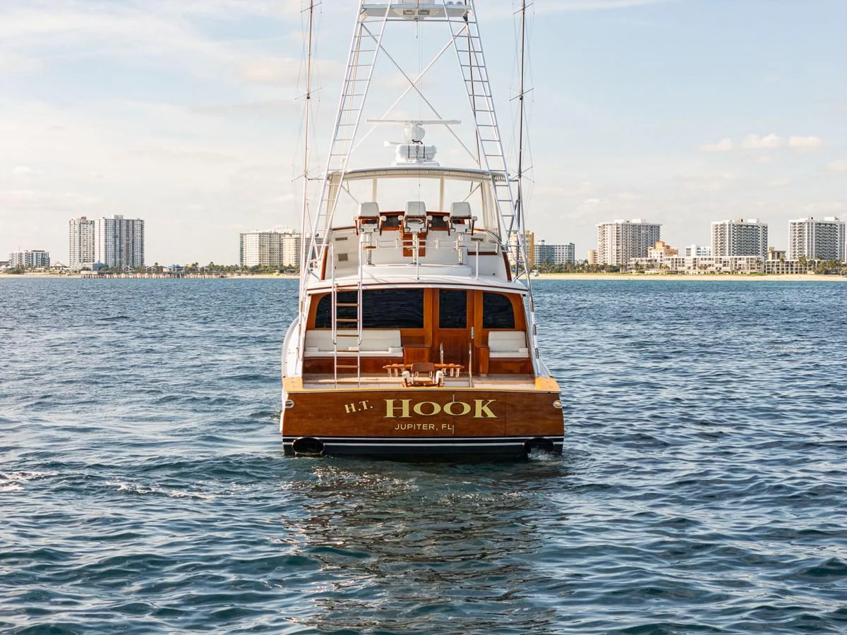A luxurious yacht is seen from the rear, cruising on calm waters with a cityscape in the background. aboard HT HOOK Yacht for Sale