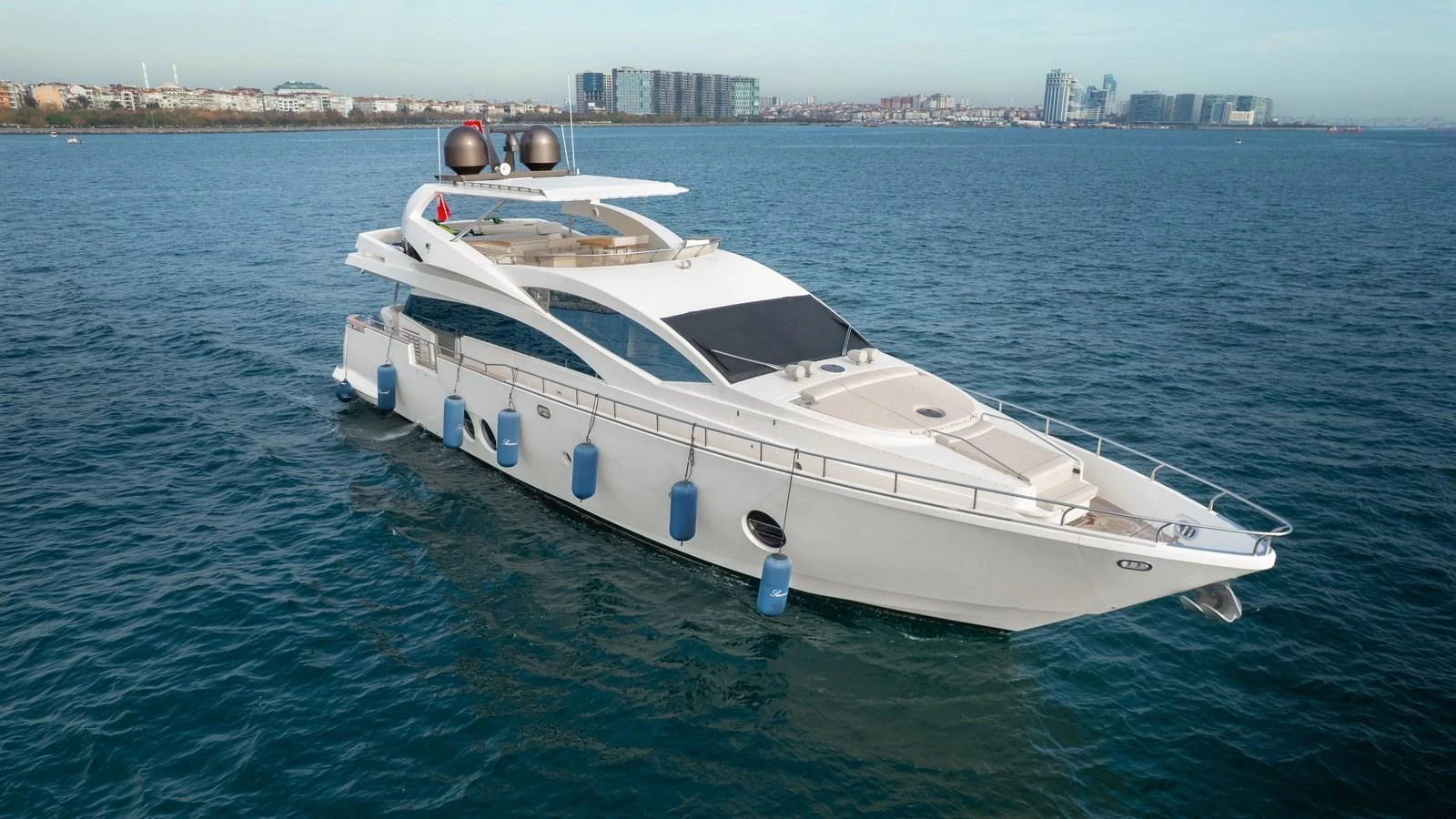 A sleek and modern yacht cruising on calm waters with a cityscape in the background. aboard SEA PEARL 2 Yacht for Sale