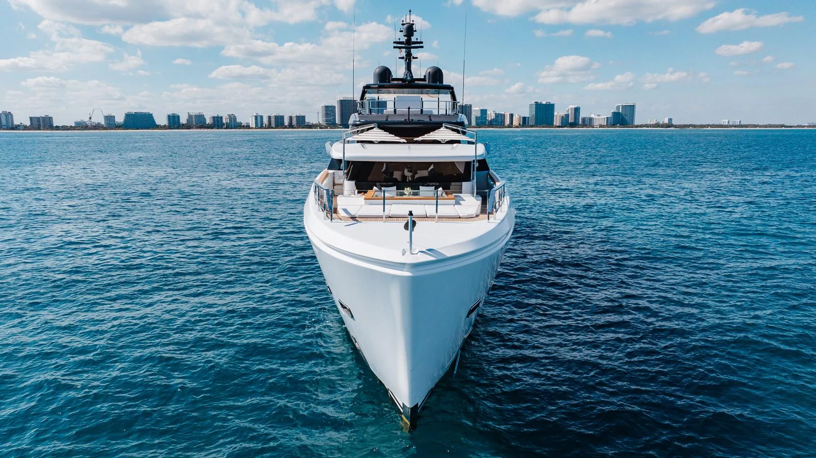 A sleek yacht cruises on calm waters with a cityscape in the background. aboard NEVERLAND II Yacht for Sale