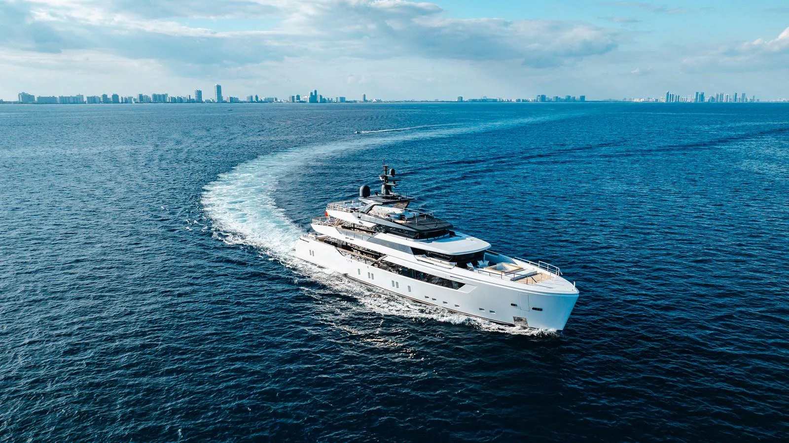 A sleek and modern yacht cruises through open waters with a city skyline in the distance. aboard NEVERLAND II Yacht for Sale