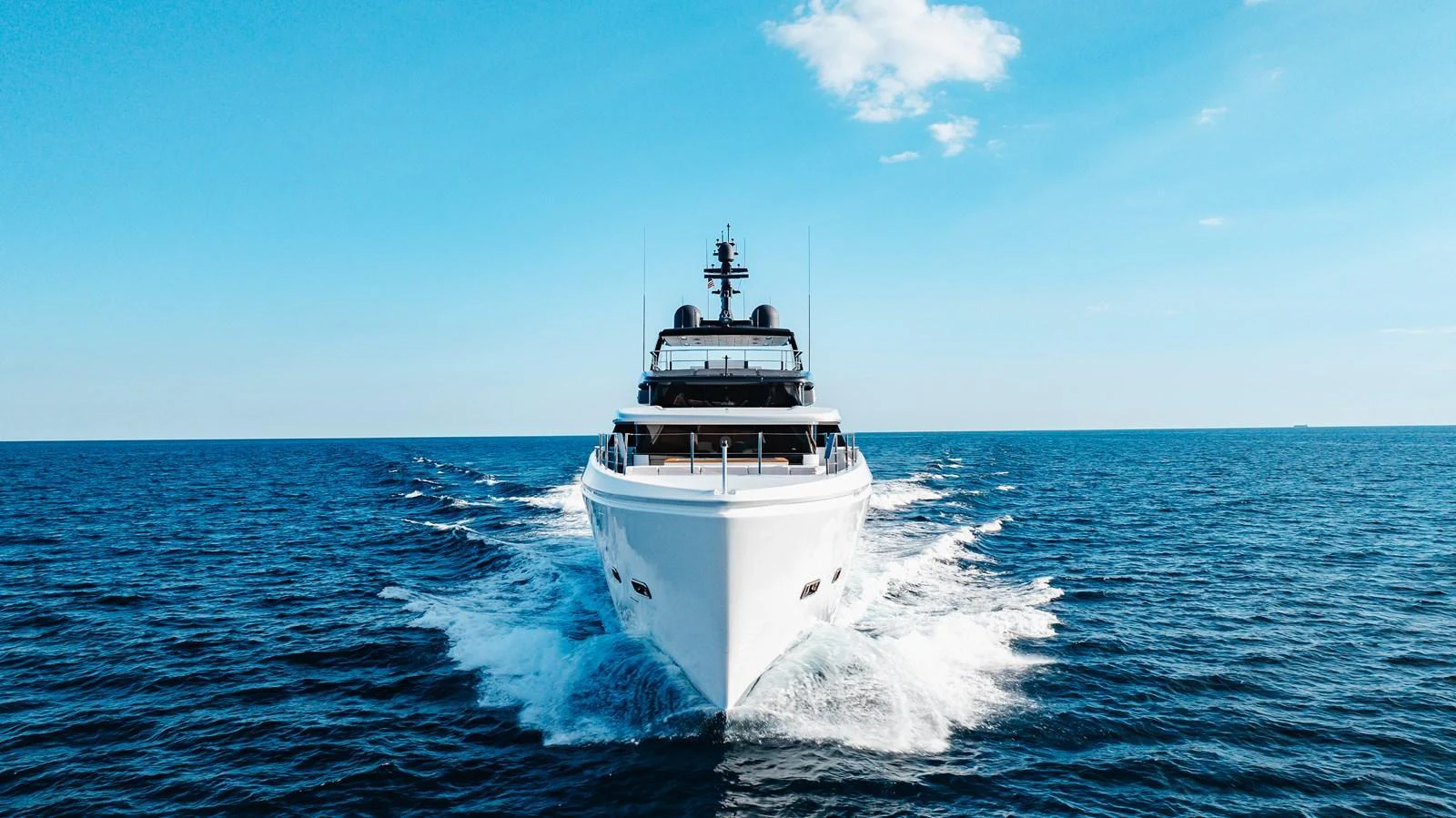 A sleek yacht cruises forward on open water under a clear blue sky. aboard NEVERLAND II Yacht for Sale