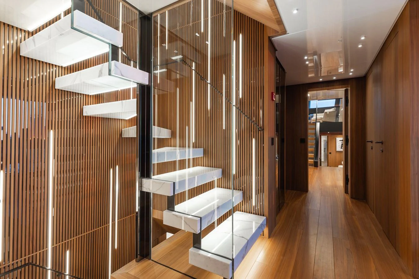 The yacht's interior features a modern staircase with glass steps and sleek wooden paneling. aboard NEVERLAND II Yacht for Sale