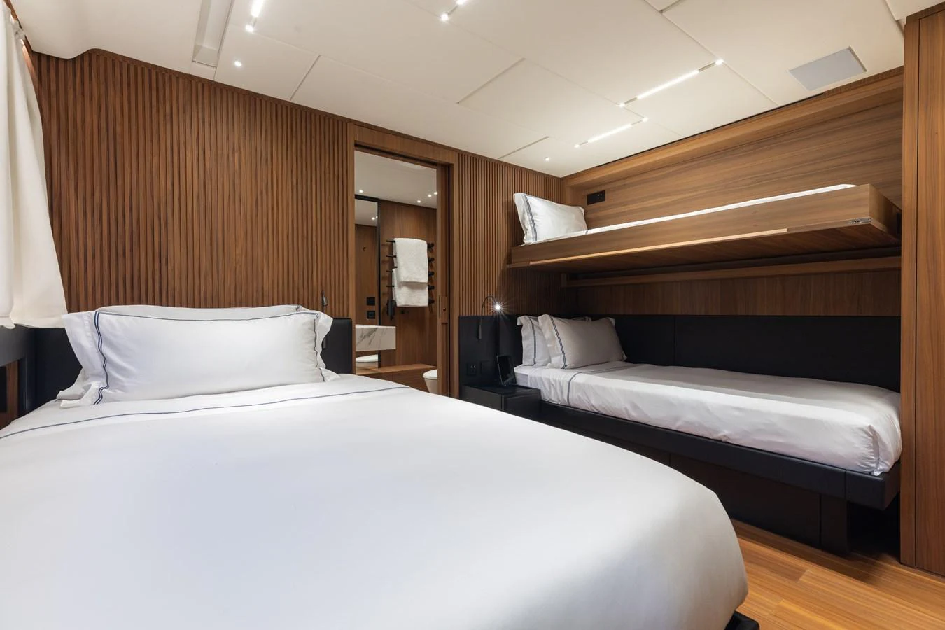 The guest stateroom features a double bed and a single bunk bed with elegant wood paneling and modern lighting. aboard NEVERLAND II Yacht for Sale