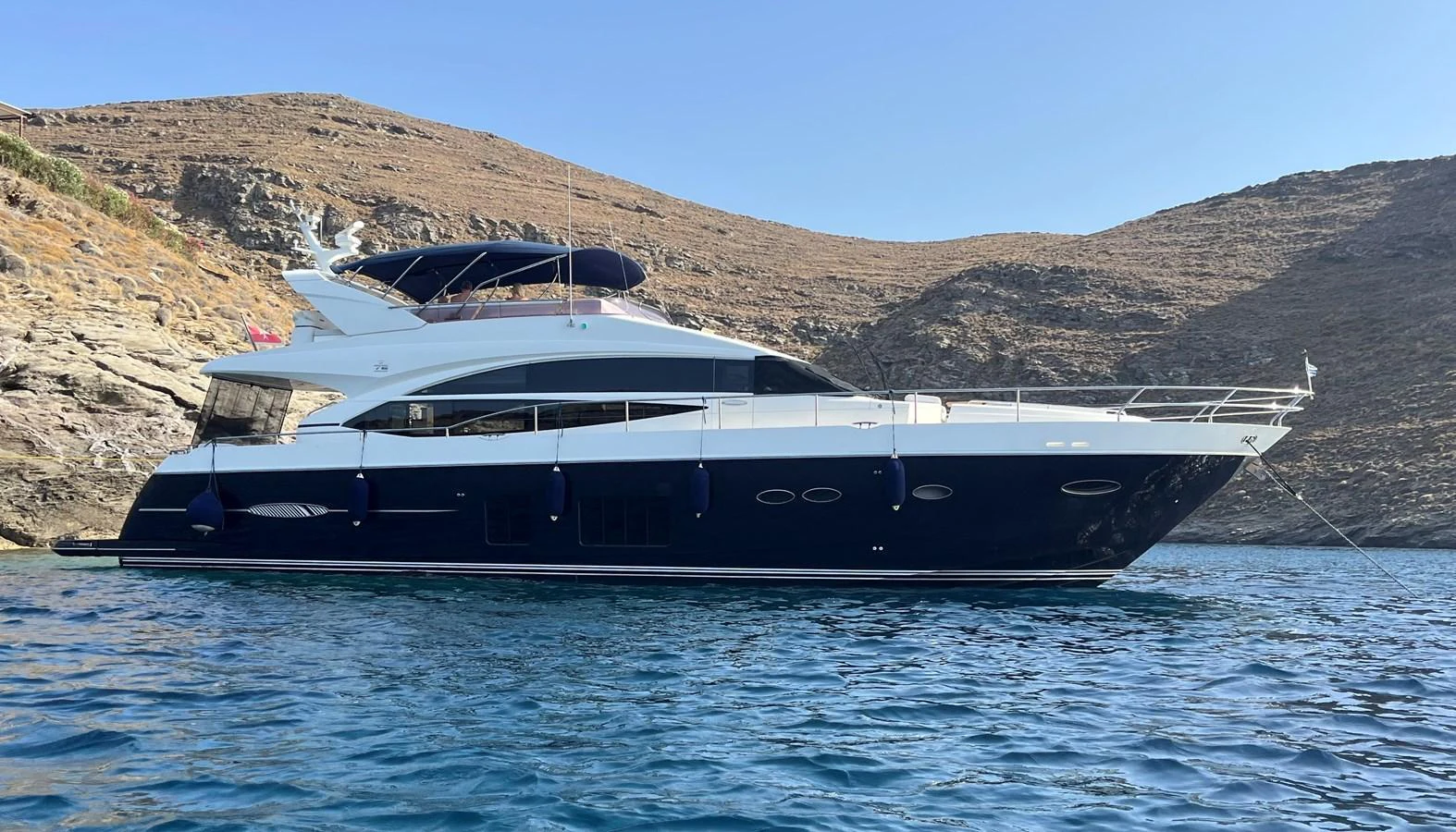 A sleek and modern yacht is anchored in a serene, rocky cove under a clear blue sky. aboard LAVIMAR II Yacht for Sale