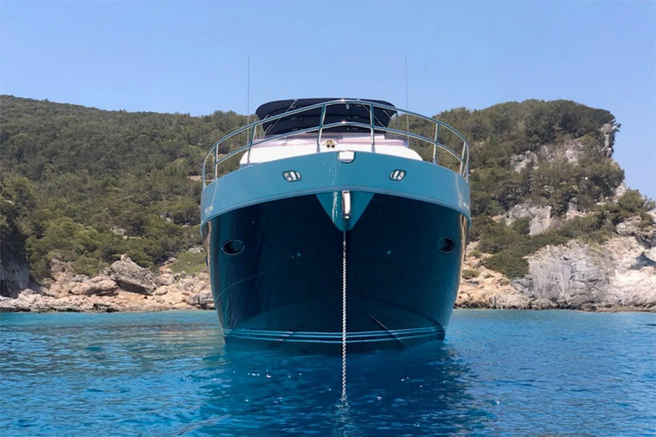 A sleek yacht is anchored in a serene, clear blue bay with lush greenery in the background. aboard LAVIMAR II Yacht for Sale