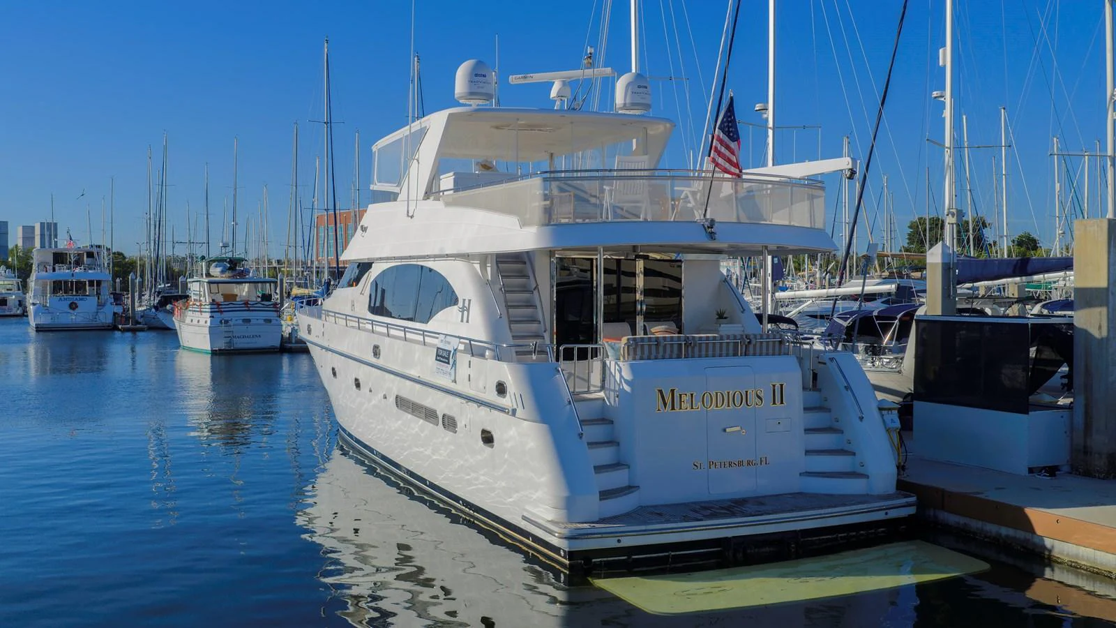 A luxurious yacht docked at a marina, showcasing its elegant aft deck and sleek design. aboard MELODIOUS LL Yacht for Sale