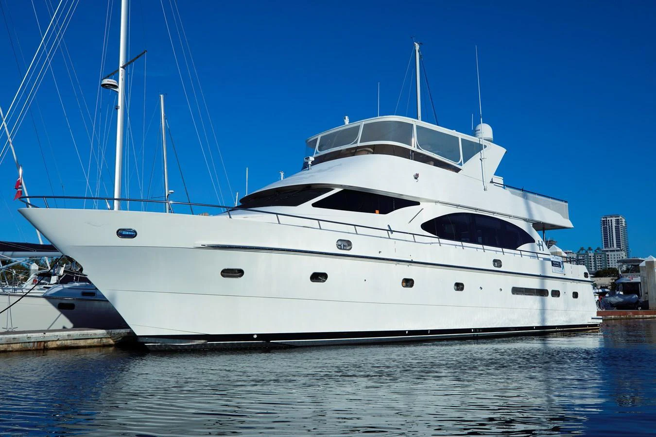 A sleek white yacht is docked at a marina under a clear blue sky. aboard MELODIOUS LL Yacht for Sale