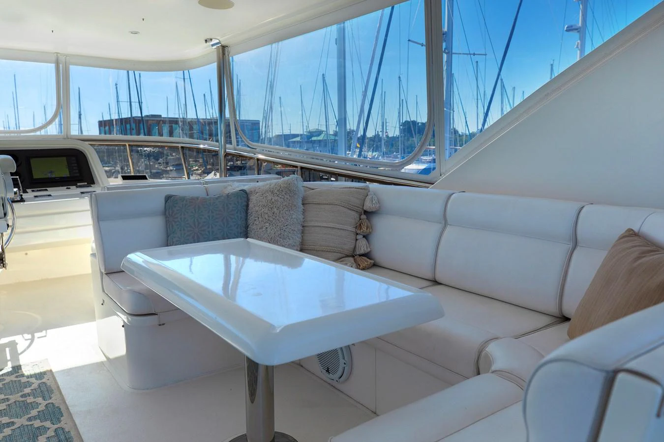 The yacht's salon features a comfortable seating area with plush cushions and a table, offering a panoramic view of the marina. aboard MELODIOUS LL Yacht for Sale