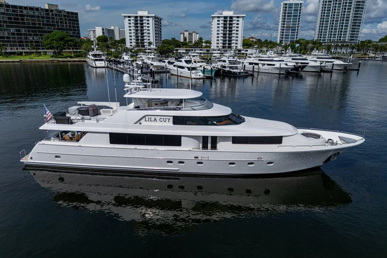 A sleek and modern yacht is docked in a marina with a cityscape in the background. aboard LILA CUY Yacht for Sale