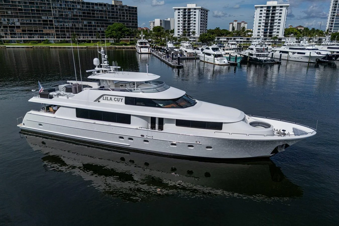 A sleek and modern yacht is docked in a marina with a backdrop of high-rise buildings. aboard LILA CUY Yacht for Sale