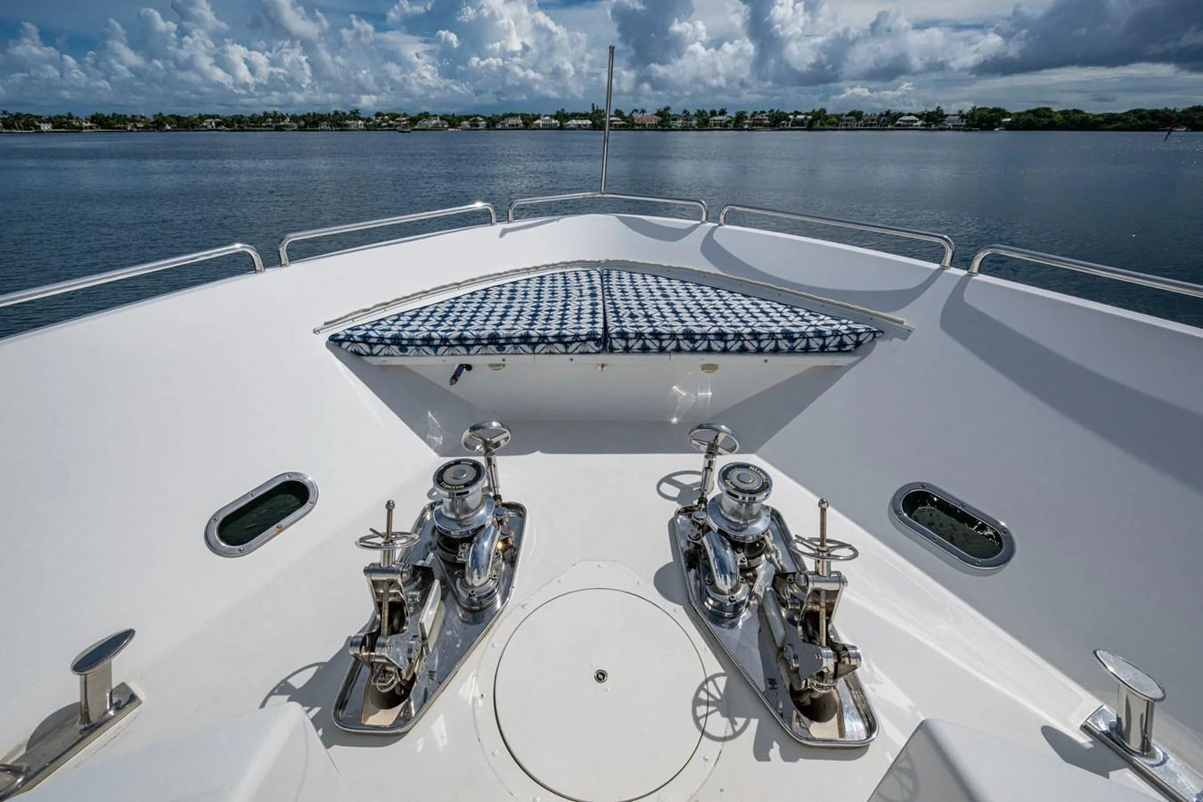 The foredeck features polished winches and a patterned sunpad, offering a serene view of the water. aboard LILA CUY Yacht for Sale